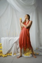 Woman stands in a studio holding a lemon while facing a table decorated with candles and surrounded