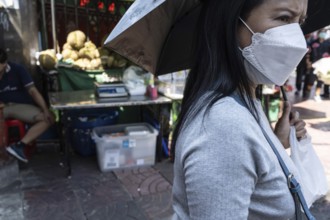 Bangkok, Thailand. March 25th 2025. A local woman with an umbrella and wearing a mask due to