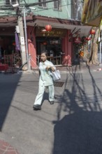 Bangkok, Thailand. March 25th 2025. A local women walking past Chinese restaurants and the shadows
