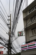 A mess of tangled wires and cables attached to a telegraph pole outside a 7 Eleven store in