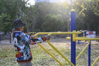Bangkok, Thailand. March 4th 2025. An elderly lady uses the public outdoor gym exercise machines in