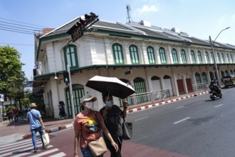 Bangkok, Thailand. March 25th 2025. People crossing the street with masks and an umbrella due to