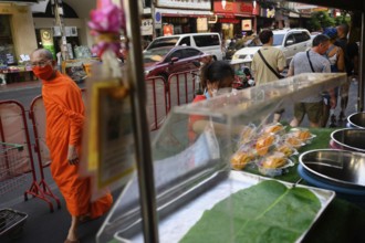 Bangkok, Thailand. February 18th 2025. A Buddhist monk walks past street food stalls along a