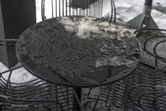 Thaw, remnants of snow on a bistro table outside during thaw in front of a café, Bavaria, Germany