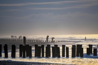 Winter on the North Sea, sunset at sea, beach walkers, coastal protection, through wooden posts,