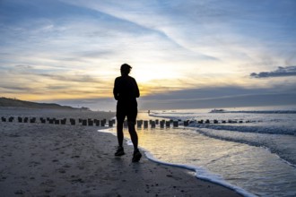 Winter on the North Sea, sunset at the beach, joggers, beach walkers, coastal protection, through