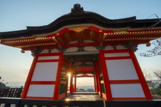 Sunset over the city with sun stars, view through the red Nishimon Gate, Kiyomizu-dera Temple, in