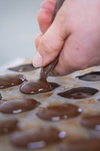 Close-up of a hand filling chocolate molds with chocolate, vegan chocolates production,