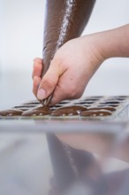 A hand injects chocolate into a mold to produce chocolates, vegan chocolates production,
