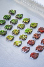 Chocolates in intense colors, decorated in leaf shapes, lie on a surface, vegan chocolates