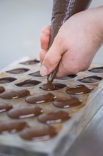 Close-up of a hand filling chocolate mold with liquid chocolate, vegan chocolates production,