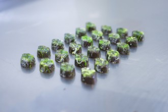 Numerous chocolates with green decorations on a smooth surface, vegan chocolates production,
