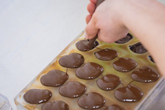 Hand with piping bag fills liquid chocolate in chocolate shape on a table, vegan chocolates