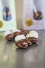 Close-up of white and brown chocolate almonds with packaging in the background, Easter production
