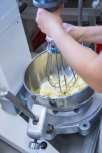 A person uses a mixer in a silver bowl to mix ingredients, vegan cake production, Haselstaller Hof,