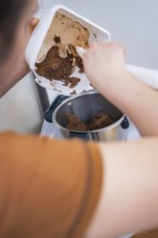 Person scrapes chocolate mix into a food processor, vegan cake production, Haselstaller Hof,