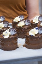 Person carrying tray with small, decorated chocolate cakes, vegan cake production, Haselstaller