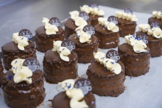 Several chocolate cakes on a tray, decorated with cream and logos, vegan cake production,