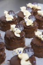 Small chocolate cakes with cream and chocolate logo on tray, vegan cake production, Haselstaller