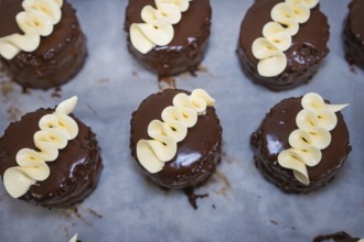 Several small chocolate cakes with white chocolate decoration on a tray, vegan cake production,