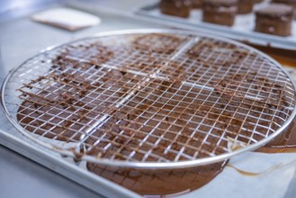 A metal grid with rotating chocolate grids, kitchen appliances in the background, vegan cake