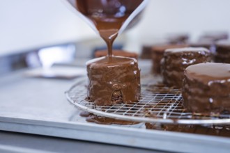 A pastry covered with liquid chocolate drips on a grid in a baking quality kitchen, vegan cake