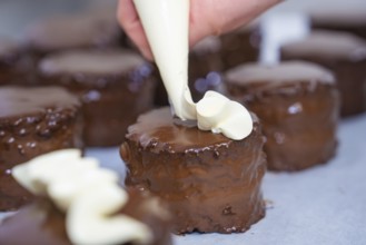 Several chocolate cakes are decorated with cream from a piping bag, Vegan Tart Production,