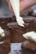 A cake is decorated with cream while several chocolate cakes are waiting, Vegan Tartchen