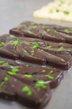 Close-up of dark chocolate bars with green patterns on a table, vegan chocolate production,