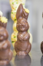 Happy chocolate bunny with flower decoration, standing upright on metal surface, Easter production