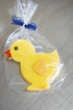 Yellow duck cookie with orange beak, wrapped in transparent film with blue ribbon, Easter