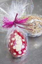 Red and white dotted Easter egg with purple ribbon wrapped in transparent film on metal surface,