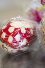 Red and white dotted Easter egg wrapped in plastic film on a metallic surface, Easter production of