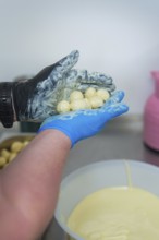Person holding chocolates over a white bowl in a kitchen, chocolate quail eggs, Easter production,