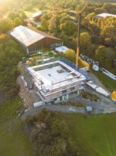 Aerial view of a construction site surrounded by forest and meadows with crane and building