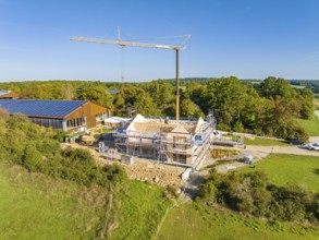 A construction site with a crane and a house under construction, surrounded by green nature and