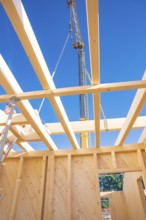 Wooden beams and a crane under a bright blue sky in a construction site, timber house construction,