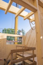 Timber frame construction with a worker on a ladder in sunny weather, timber house construction,