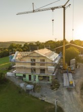 House construction with a crane and scaffolding in a rural area at sunset, timber house