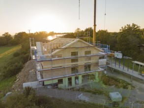 Building under construction at sunset, surrounded by scaffolding in a rural area, timber house