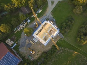 Bird's eye view of a construction site with crane and semi-finished building in a green area,