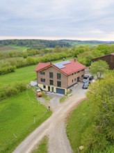 House with red roof and solar panel in rural area with green pastures and a road, Holzhausbau,
