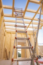 Interior view of a timber structure under construction, ladder leading upwards under blue sky,