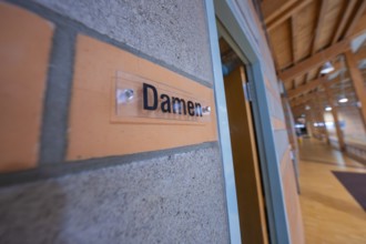 Wall with 'ladies' sign in a room with wooden elements and warm colors, Schlehengäu Sporthalle