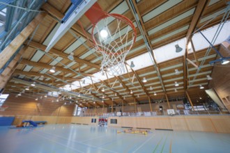 Basketball hoop in a large sports hall with wooden structure and floor markings, Schlehengäu