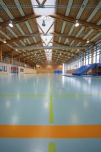 View of an empty sports hall with marked playing fields and glowing ceiling lamps, Schlehengäu
