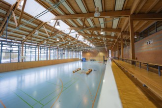 Spacious, bright sports hall with visible wooden roof and large window fronts along the walls,
