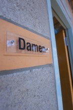 Close-up of a sign with the words' ladies' on a concrete wall next to a door, Schlehengäu