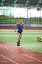 Woman running on a track in a stadium wearing a blue jersey, middle distance runner Katharina