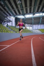 Female athlete sprints energetically on a red track in a sports complex, middle distance runner